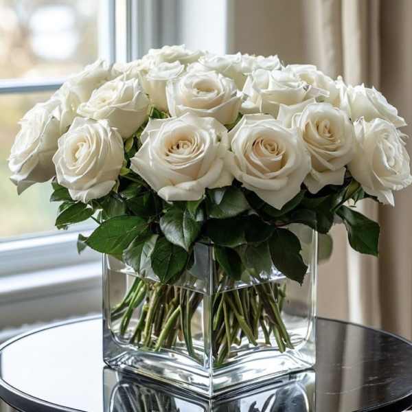 White roses arranged in a clear square glass vase