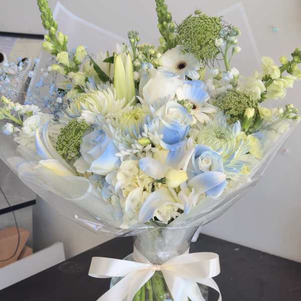 White and pale blue bouquet in a glass vase with a ribbon bow