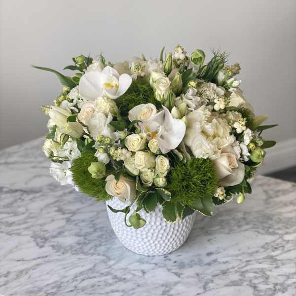 White floral arrangement in a textured white vase with green accents