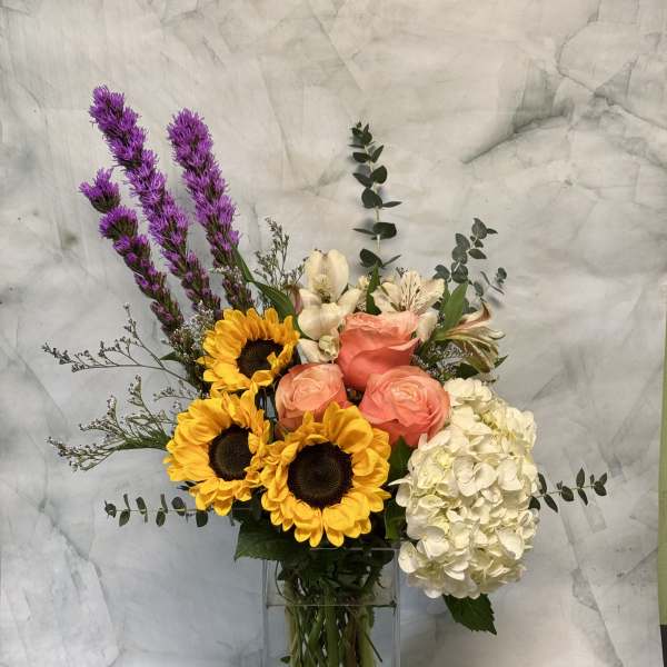 Bouquet of sunflowers, roses, and hydrangea in a glass vase