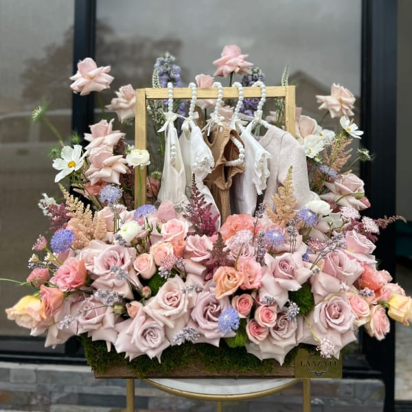Pastel rose arrangement with hanging baby clothes in a wooden frame