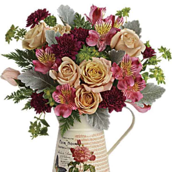 Bouquet of peach roses and burgundy flowers in a decorative pitcher vase