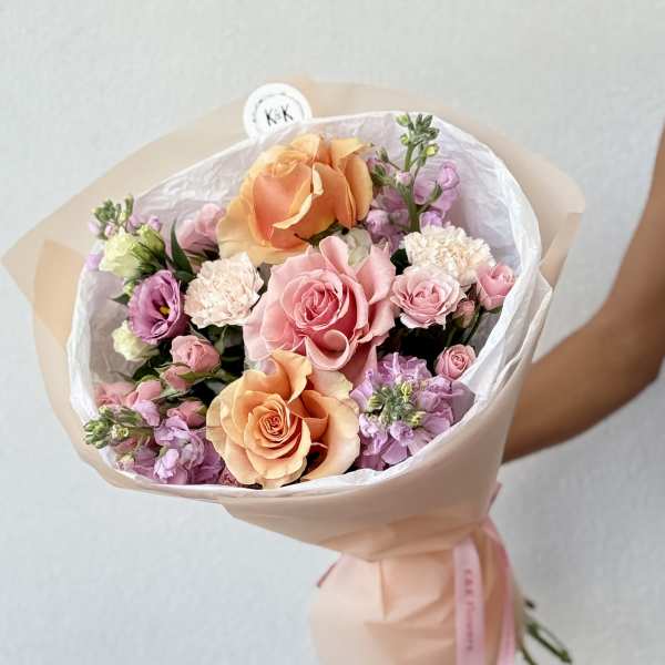 Bouquet of peach and pink roses with lavender blooms wrapped in pale paper