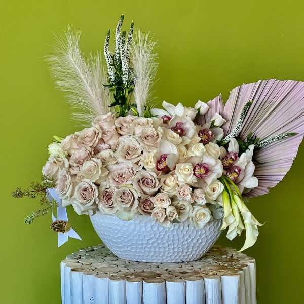 Large bouquet of pale roses and white orchids in a white bowl vase