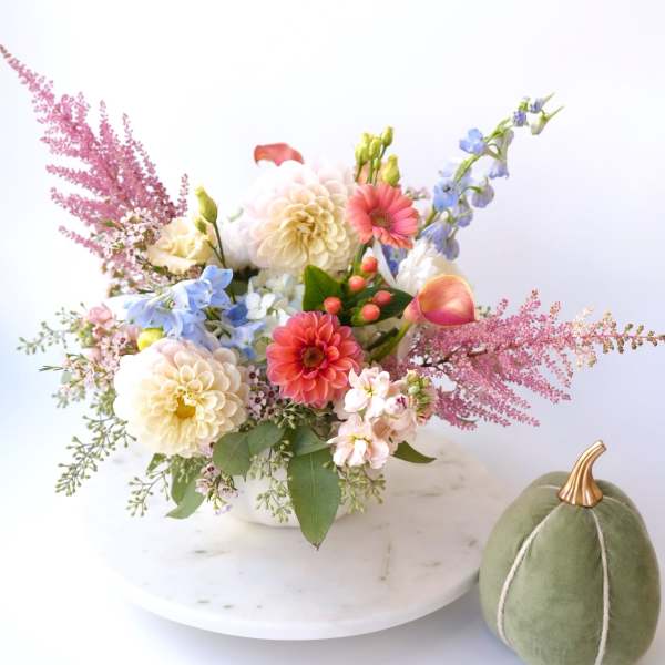 Mixed pastel flower arrangement in a white bowl with a green velvet pumpkin