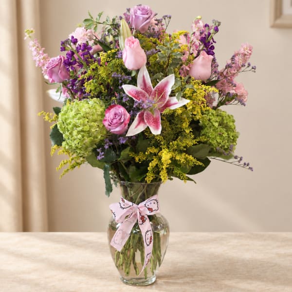 Mixed bouquet of pink and purple flowers in a clear glass vase with a ribbon