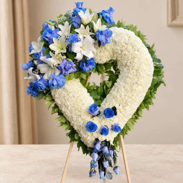 Heart-shaped floral wreath with white blooms and blue roses on an easel