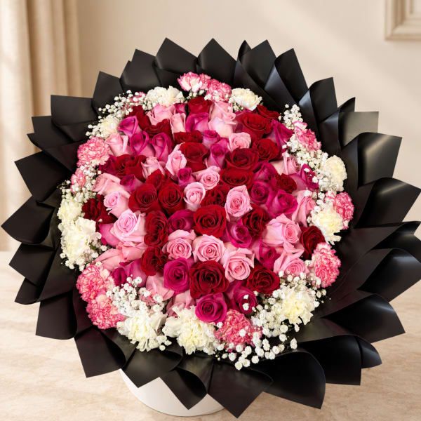 Large bouquet of red and pink roses with white filler flowers in black wrap