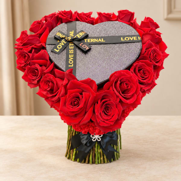 Heart-shaped box surrounded by red roses with a ribbon bow