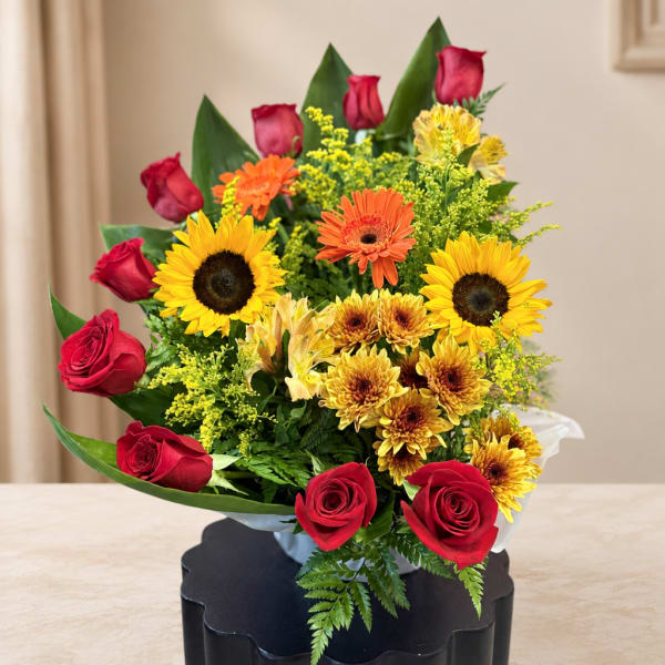 Mixed bouquet with red roses, sunflowers, and yellow-orange daisies in a vase