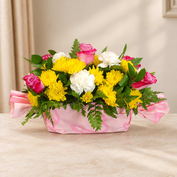 Pink roses and yellow chrysanthemums in a pink wrapped basket