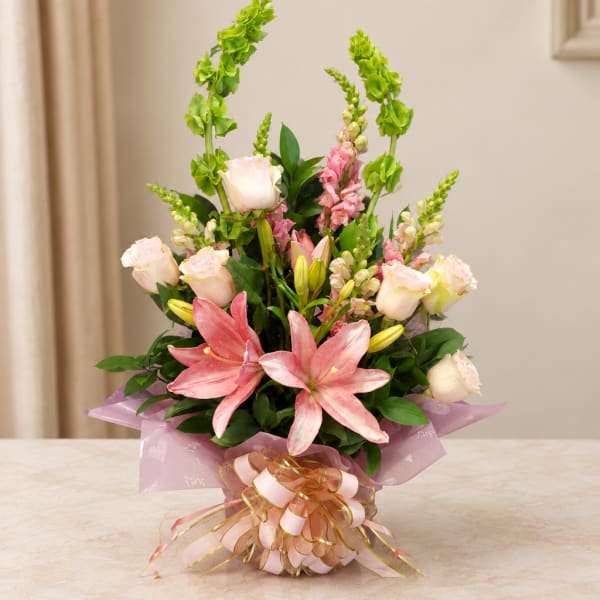 Pink lilies and pale roses arranged in a wrapped bouquet with a ribbon bow