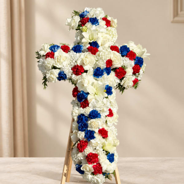 Cross-shaped floral tribute with white, red, and blue flowers on an easel