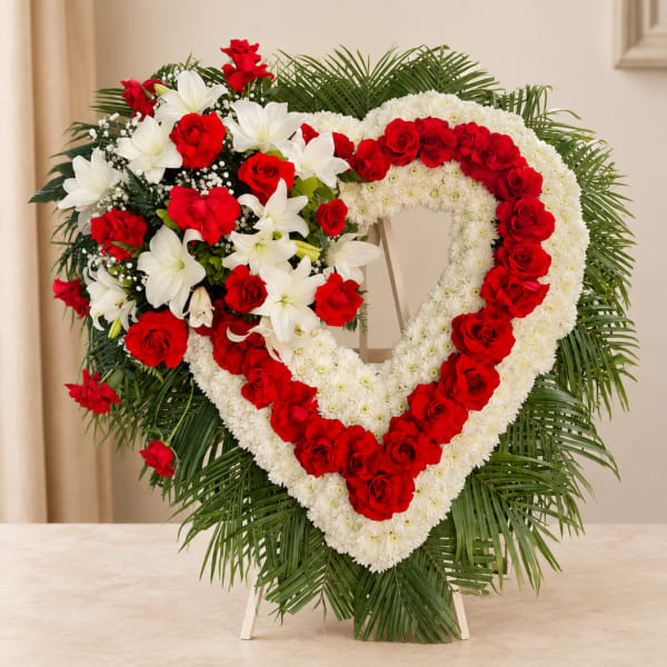 Heart-shaped floral wreath with red roses and white flowers on a stand