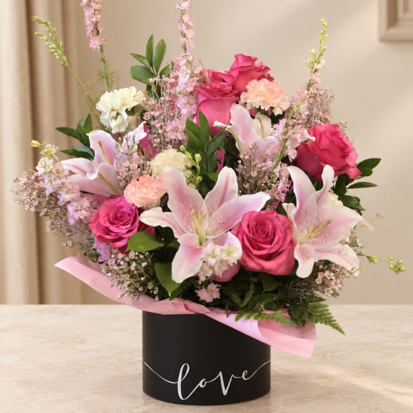 Pink roses and lilies arranged in a black box with a pink ribbon