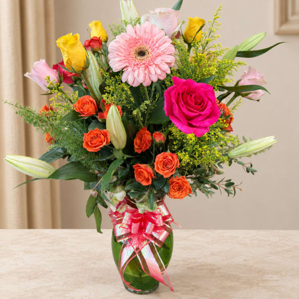 Mixed bouquet of roses, gerbera daisies, lilies, and a pink ribbon in a green vase