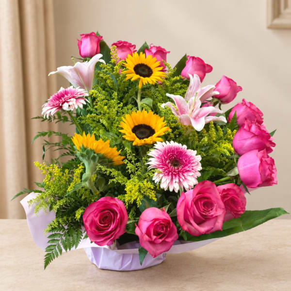 Pink roses and lilies with sunflowers in a wrapped bouquet
