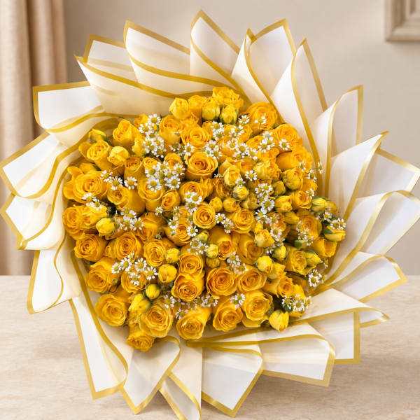 Bouquet of yellow roses with small white daisies wrapped in white paper with gold trim