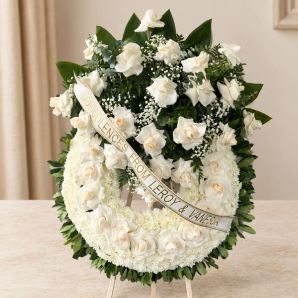 White condolence wreath with roses and a ribbon on an easel