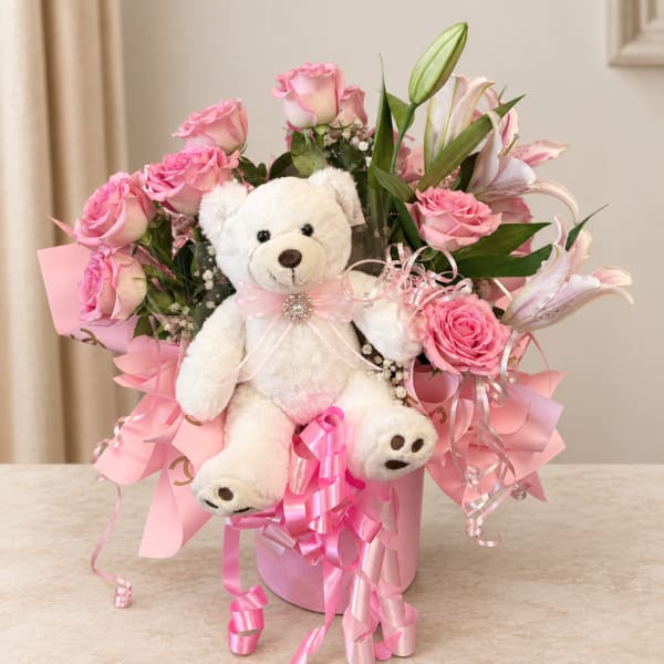 Pink roses and lilies arranged with a white teddy bear in a pink box