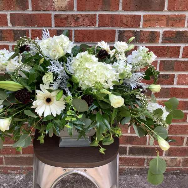 White floral arrangement in a gray vase with mixed greenery