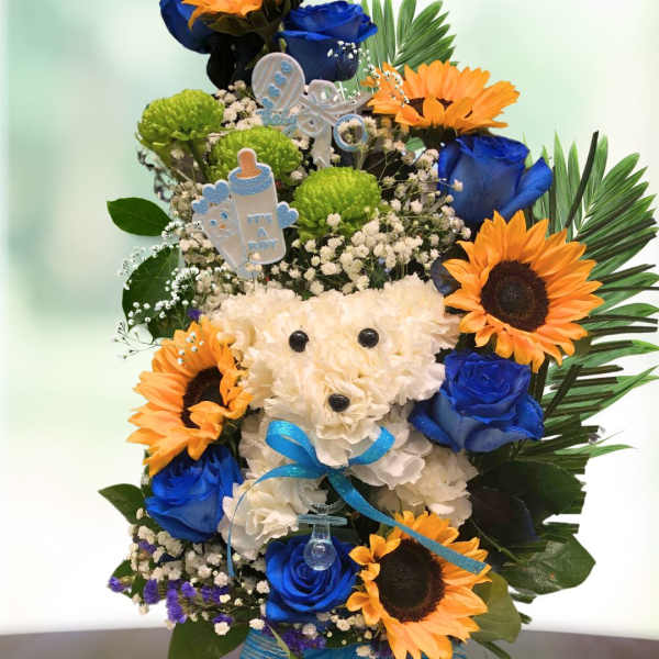 Blue roses and sunflowers arranged around a white teddy bear