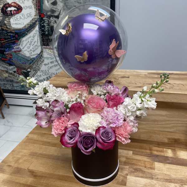 Pink and purple floral arrangement with a clear balloon and butterfly decorations