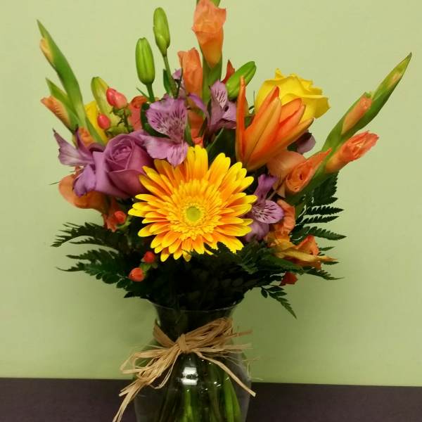 Mixed bouquet in a glass vase with yellow, orange, and purple flowers