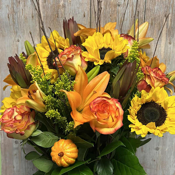Bouquet of sunflowers, orange roses, and lilies in a glass vase