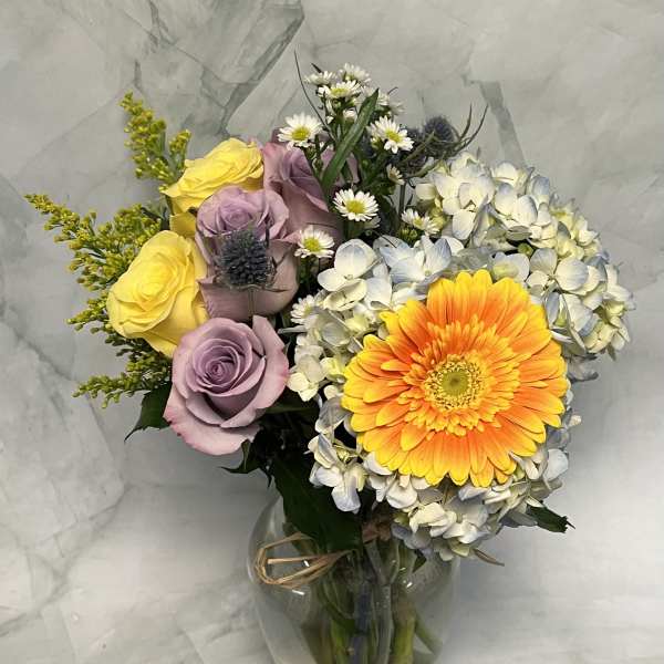 Bouquet of yellow and lavender roses with a bright orange gerbera daisy in a glass vase.