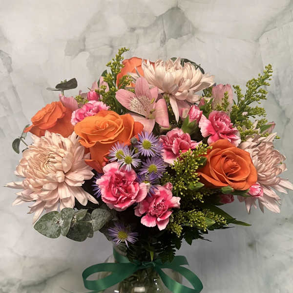 Mixed bouquet of orange roses, pink carnations, and pale chrysanthemums in a glass vase