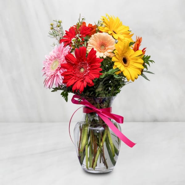 Mixed gerbera daisies in a clear glass vase with a pink ribbon