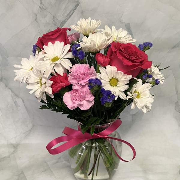 Bouquet of red roses, white daisies, and pink carnations in a glass vase