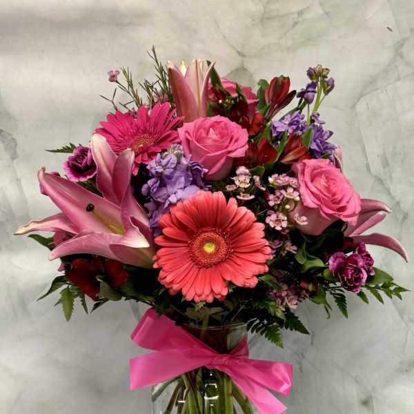 Pink and purple mixed bouquet in a glass vase with a bright ribbon