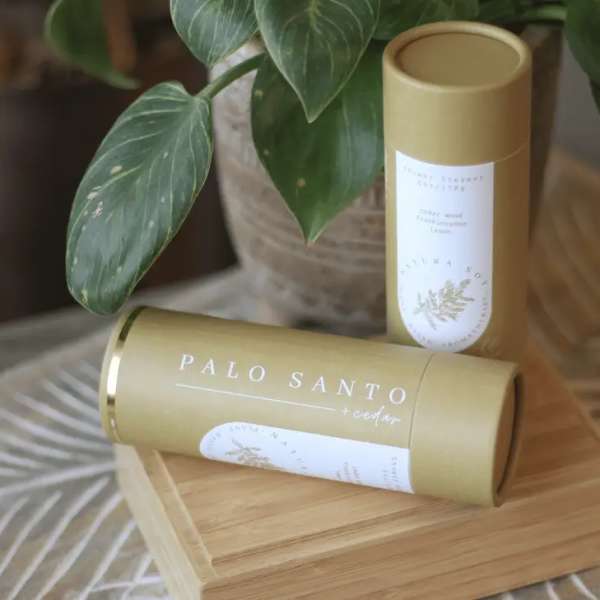 Two palo santo candles in gold tubes beside a potted plant