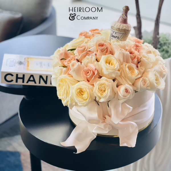 Round bouquet of pale peach and cream roses with a small champagne bottle topper