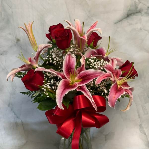 Red roses and pink lilies in a glass vase with a red ribbon