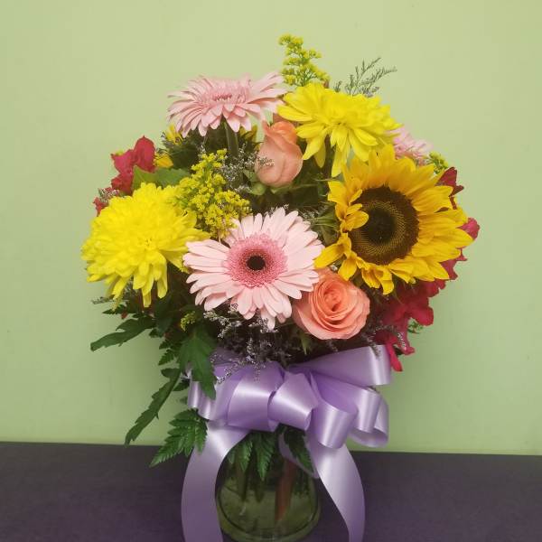 Mixed bouquet with sunflowers, pink gerberas, and roses in a glass vase