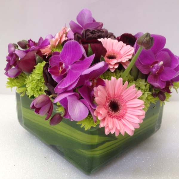 Pink gerbera daisies and purple orchids in a green glass vase