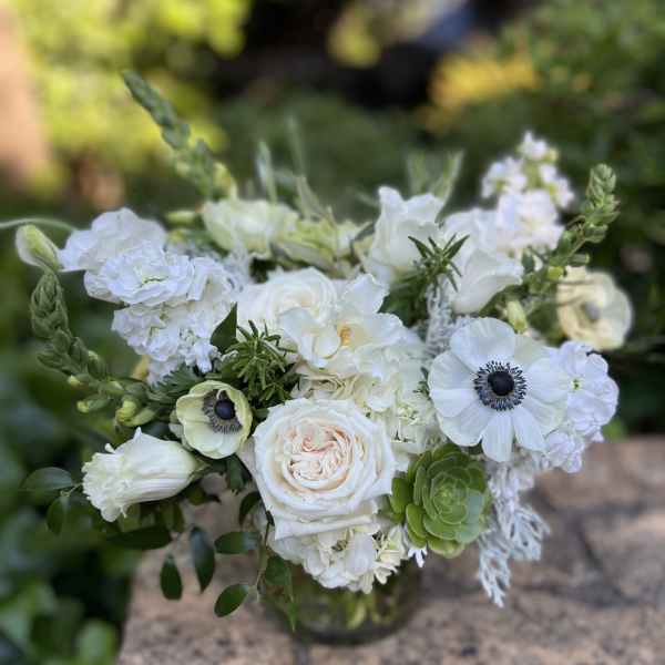 White floral bouquet in a glass vase with green accents