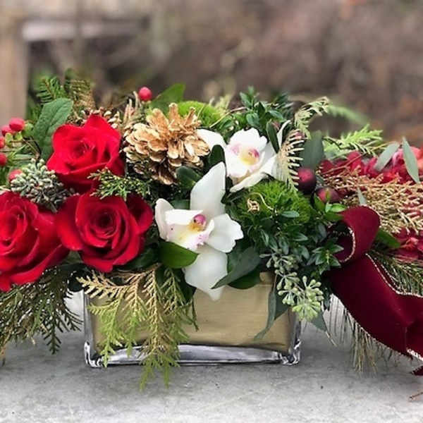 Red roses and white orchids in a glass vase with pinecones and ribbon