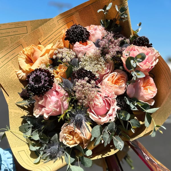 Bouquet of pink and peach roses wrapped in newspaper-style paper