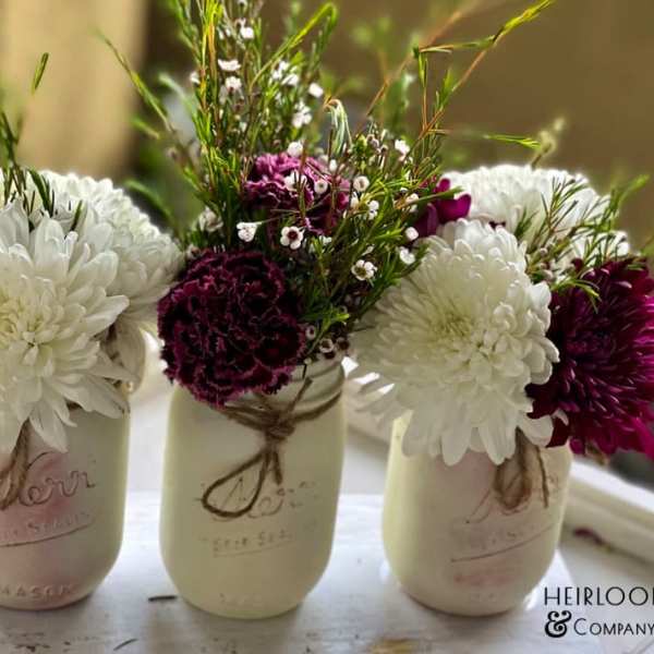 Three mason jars holding white and burgundy flowers