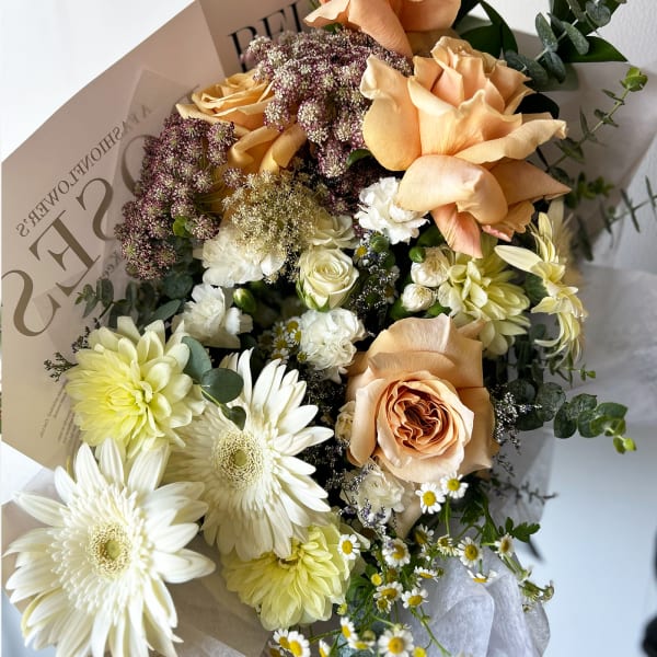 Peach roses and white daisies in a wrapped bouquet