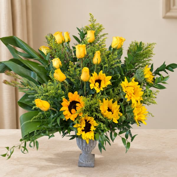 Yellow roses and sunflowers arranged in a gray vase