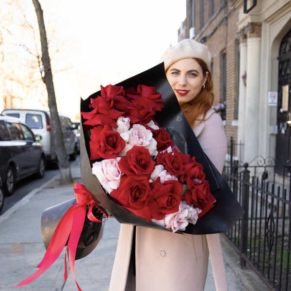 Woman holding a large bouquet of red and pale pink roses wrapped in black paper