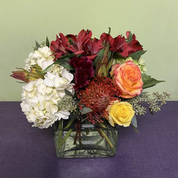 Mixed bouquet in a square glass vase with red, white, orange, and yellow flowers