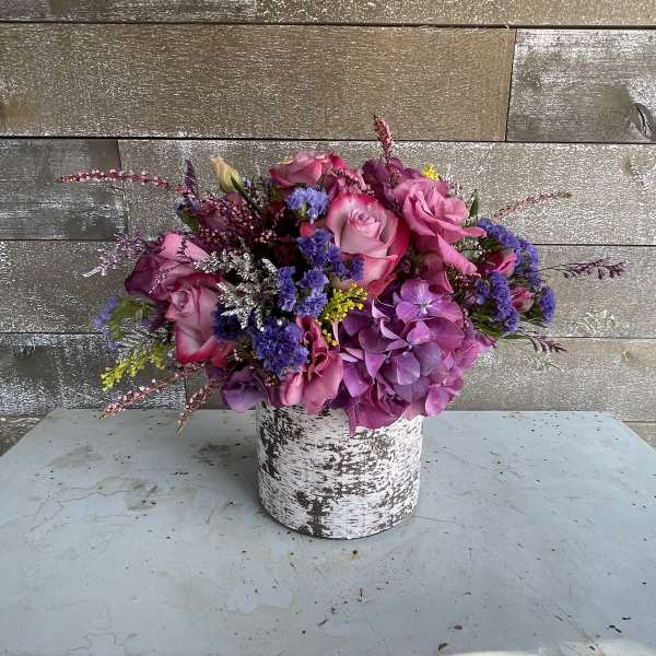 Pink and purple floral arrangement in a white textured container