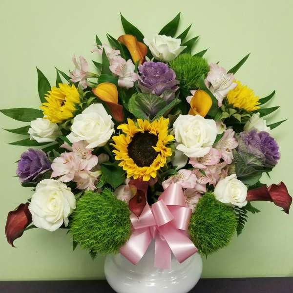 Mixed bouquet in a white vase with roses, sunflowers, and calla lilies