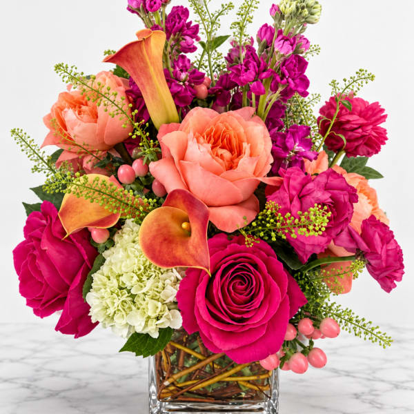 Bright mixed bouquet in a clear square vase with roses, calla lilies, and purple blooms